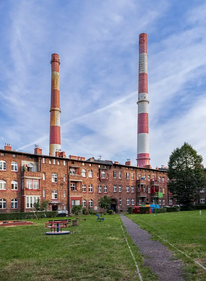 Dziedziniec familoków w Nikiszowcu, za nimi dwa kominy w czerwono-białe pasy